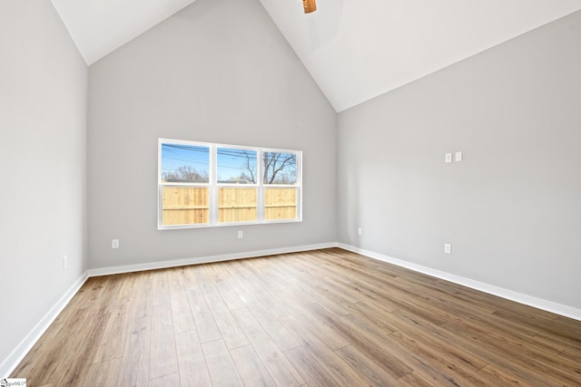 spare room with ceiling fan, high vaulted ceiling, baseboards, and wood finished floors