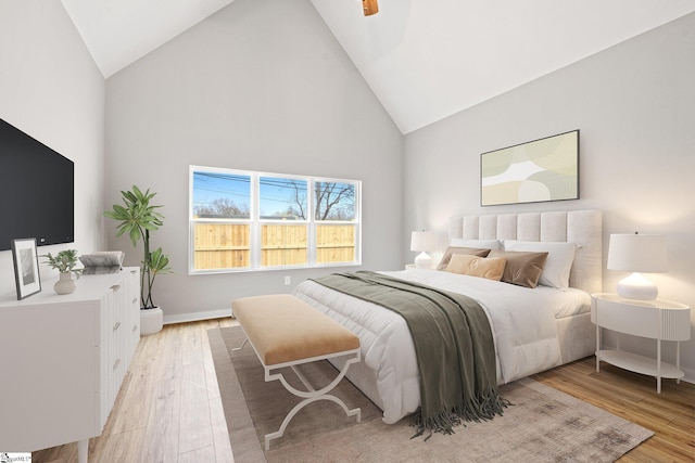 bedroom with high vaulted ceiling, light wood-type flooring, and baseboards