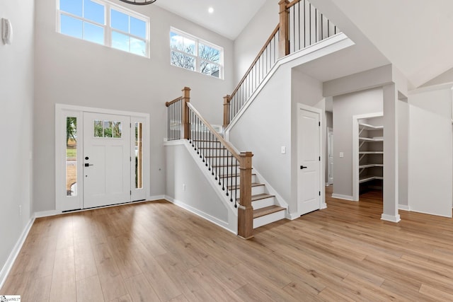 entryway featuring stairway, baseboards, a high ceiling, and light wood-style flooring