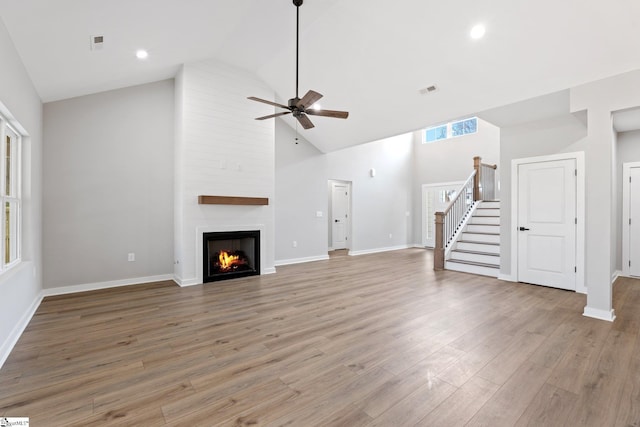 unfurnished living room featuring stairway, high vaulted ceiling, a fireplace, ceiling fan, and light wood-style floors