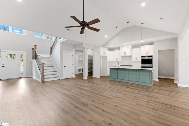 kitchen featuring open floor plan, light countertops, white cabinets, high vaulted ceiling, and a sink