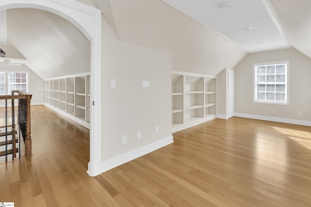 additional living space with built in features, baseboards, vaulted ceiling, and light wood finished floors