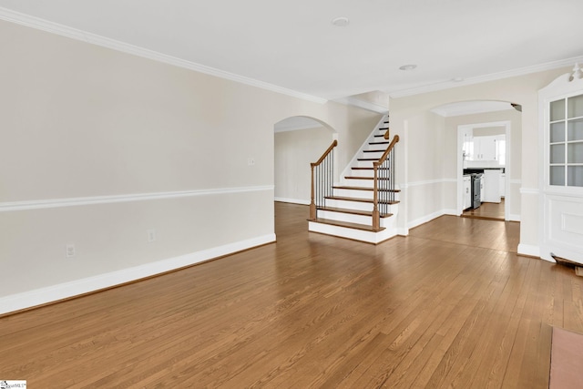 unfurnished room featuring crown molding, baseboards, stairway, arched walkways, and wood-type flooring