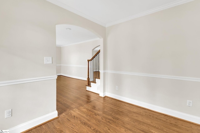 empty room with stairway, wood finished floors, baseboards, arched walkways, and crown molding