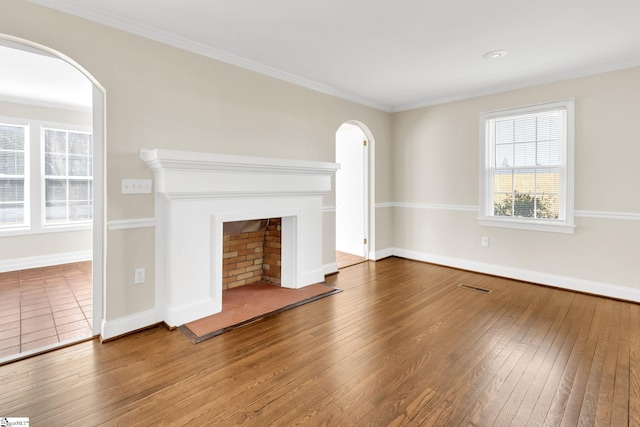 unfurnished living room featuring baseboards, visible vents, a fireplace with raised hearth, arched walkways, and wood-type flooring