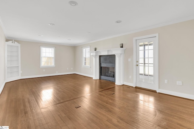 unfurnished living room with a tiled fireplace, crown molding, baseboards, and wood finished floors