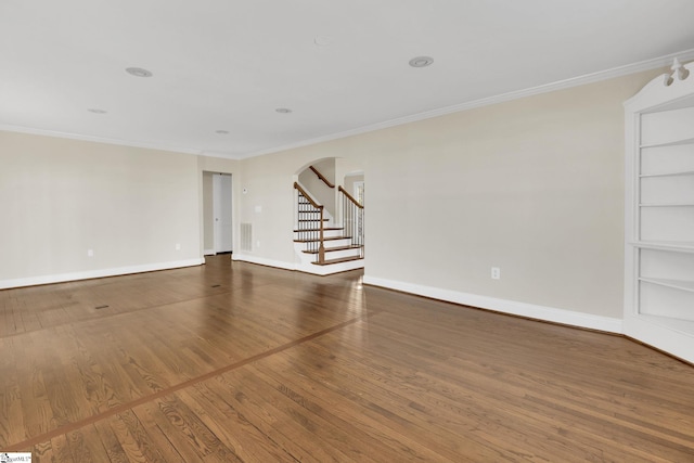 spare room featuring arched walkways, wood finished floors, stairs, and ornamental molding