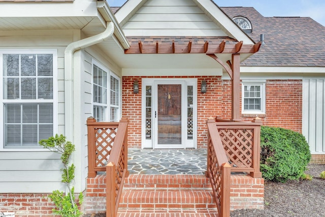 doorway to property featuring brick siding and roof with shingles