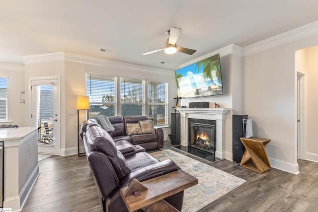 living area with a fireplace with flush hearth, ornamental molding, baseboards, ceiling fan, and dark wood-style flooring