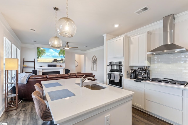 kitchen featuring visible vents, open floor plan, appliances with stainless steel finishes, wall chimney exhaust hood, and a sink