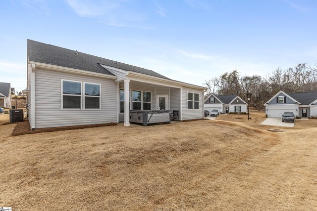 back of property featuring central AC unit, a hot tub, a lawn, and roof with shingles