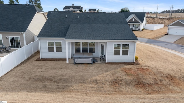 rear view of house with a hot tub, a fenced backyard, and roof with shingles