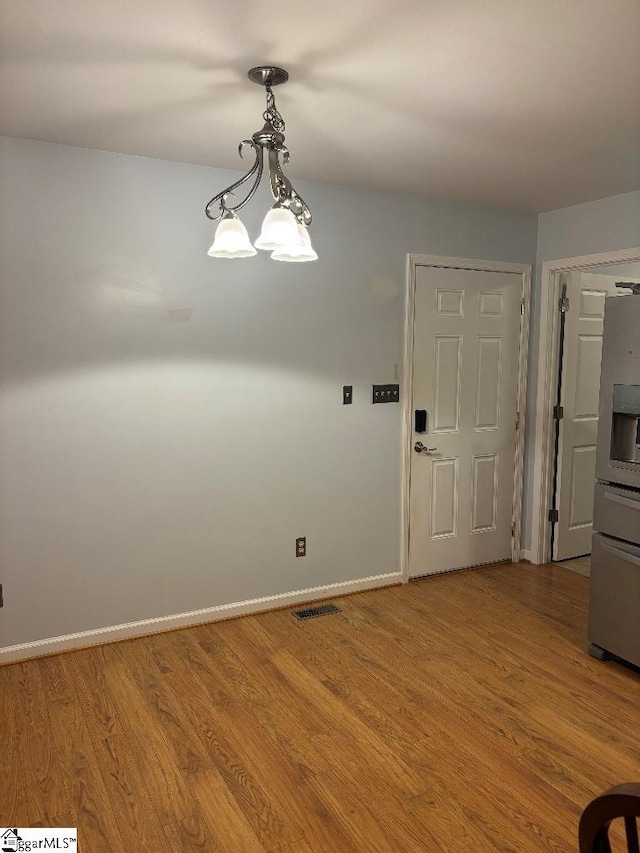 unfurnished dining area featuring wood finished floors, visible vents, a chandelier, and baseboards