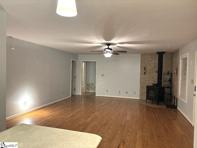 unfurnished living room featuring visible vents, a ceiling fan, wood finished floors, baseboards, and a wood stove