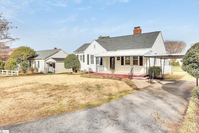 view of front of property featuring roof with shingles, covered porch, a chimney, and fence