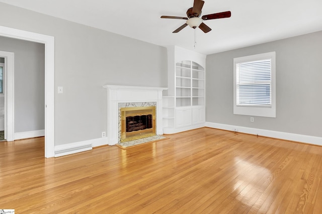 unfurnished living room with light wood-style flooring, a fireplace, a ceiling fan, and baseboards