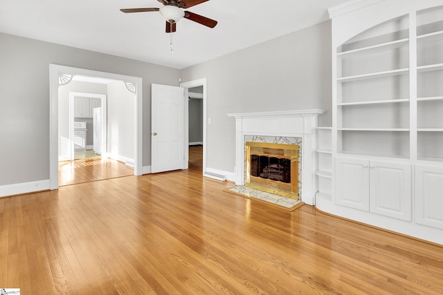 unfurnished living room with baseboards, built in features, light wood-style flooring, a fireplace, and a ceiling fan