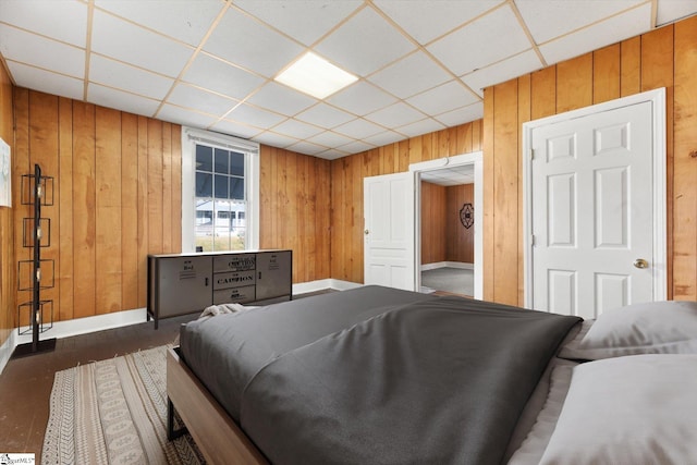 bedroom with wooden walls, dark wood-type flooring, baseboards, and a drop ceiling