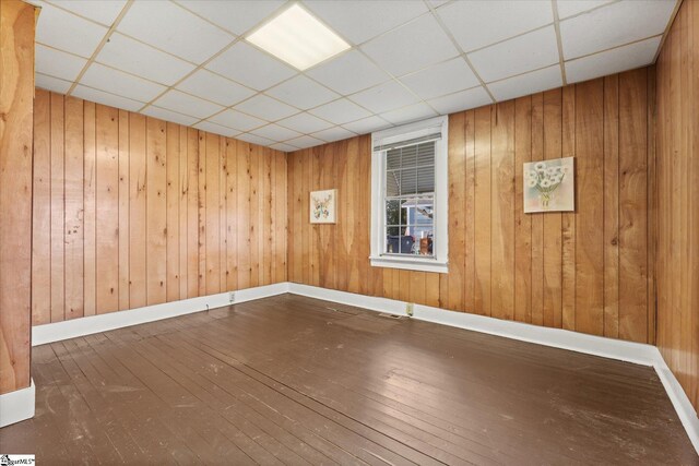 empty room with visible vents, wood walls, baseboards, and hardwood / wood-style floors