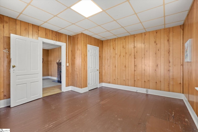 unfurnished room with a drop ceiling, baseboards, hardwood / wood-style floors, and wood walls