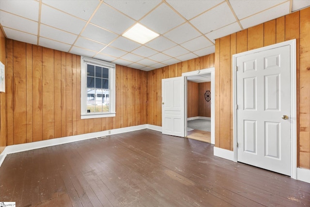 unfurnished room with wood walls, a paneled ceiling, baseboards, and hardwood / wood-style floors