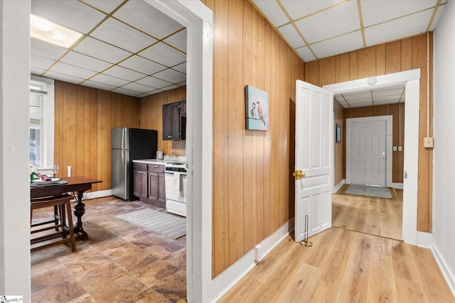 hall featuring light wood-type flooring, a paneled ceiling, baseboards, and wood walls