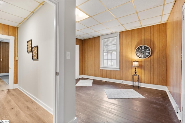 hallway with a drop ceiling, wood finished floors, baseboards, and wood walls