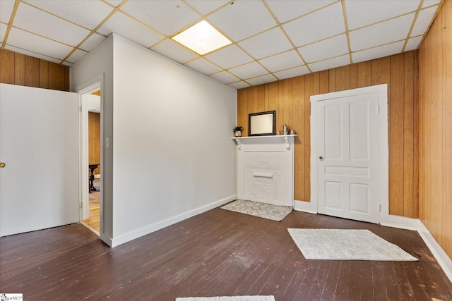 interior space with a drop ceiling, wood-type flooring, baseboards, and wood walls