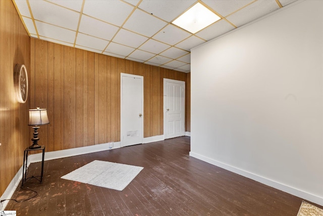 empty room featuring a drop ceiling, baseboards, hardwood / wood-style floors, and wood walls