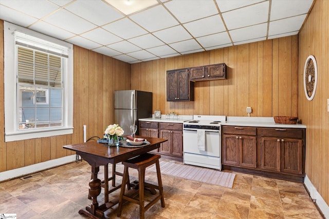 kitchen featuring white electric stove, visible vents, wooden walls, and freestanding refrigerator