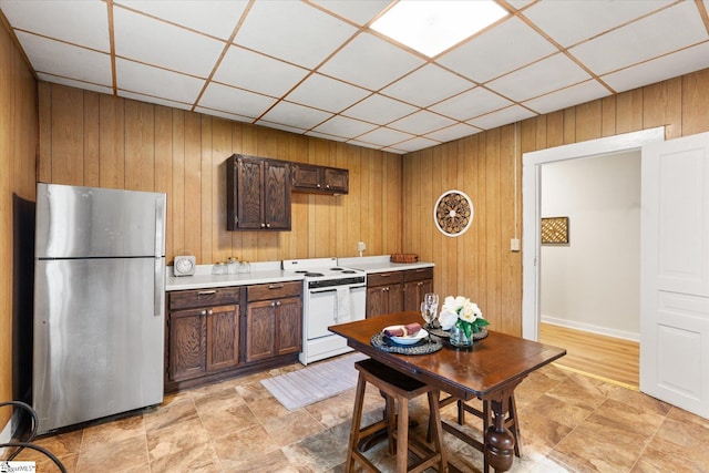 kitchen featuring a drop ceiling, white range with electric stovetop, freestanding refrigerator, wooden walls, and light countertops