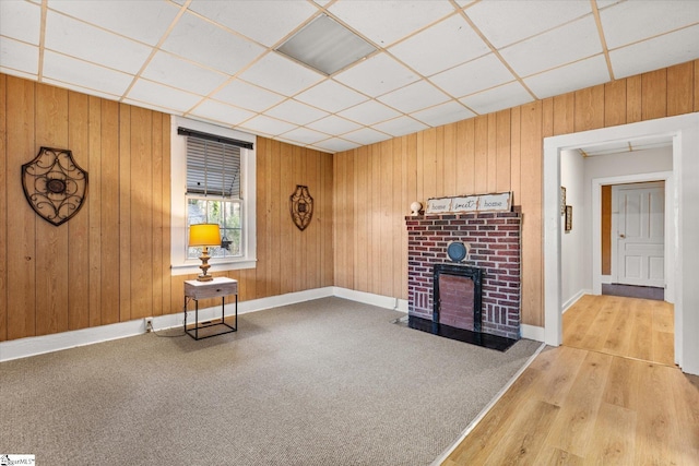 unfurnished room featuring a drop ceiling, wood walls, baseboards, and carpet