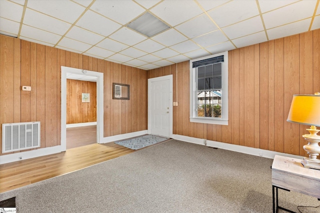 interior space featuring visible vents, a paneled ceiling, wooden walls, and baseboards