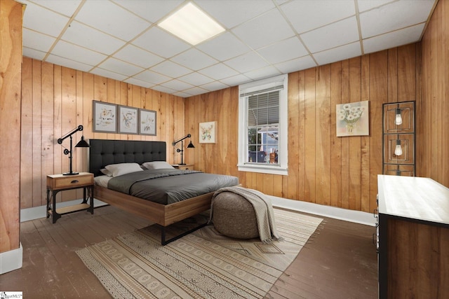 bedroom with a drop ceiling, wood walls, baseboards, and hardwood / wood-style floors