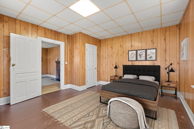 bedroom featuring wooden walls, a paneled ceiling, baseboards, and wood finished floors