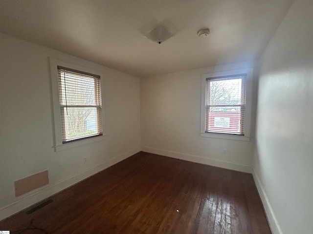 spare room featuring a wealth of natural light, visible vents, dark wood finished floors, and baseboards