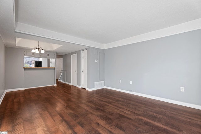 unfurnished living room with visible vents, a raised ceiling, dark wood finished floors, baseboards, and a chandelier