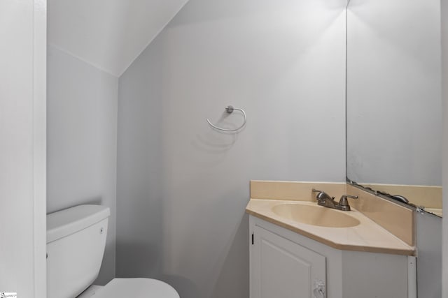 half bath with vanity, vaulted ceiling, and toilet