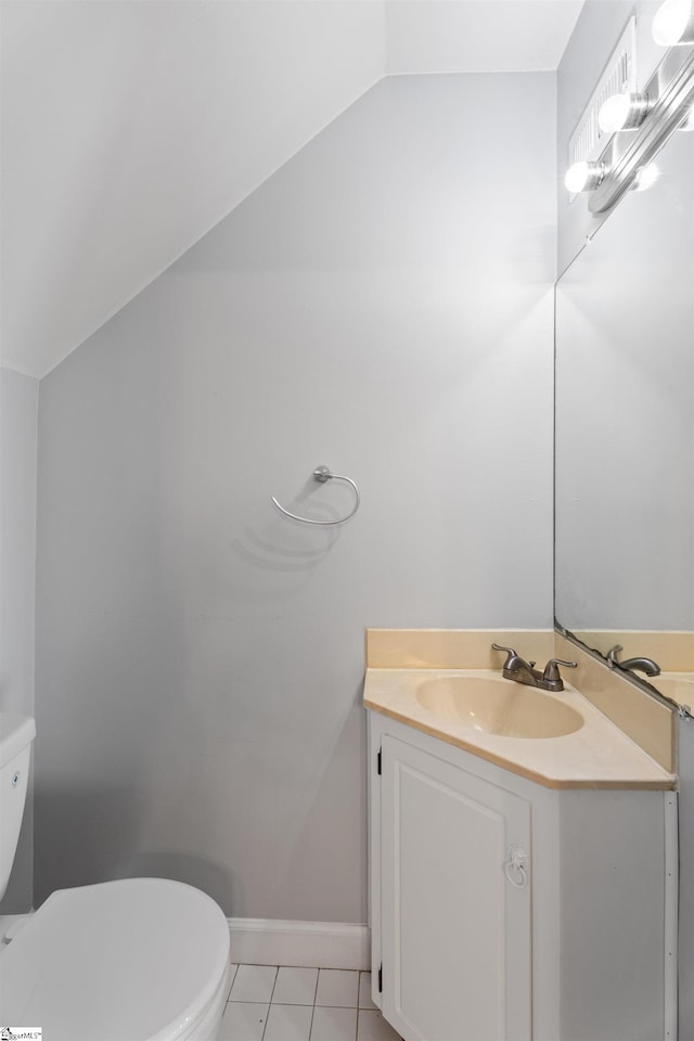 bathroom featuring vanity, baseboards, lofted ceiling, tile patterned floors, and toilet