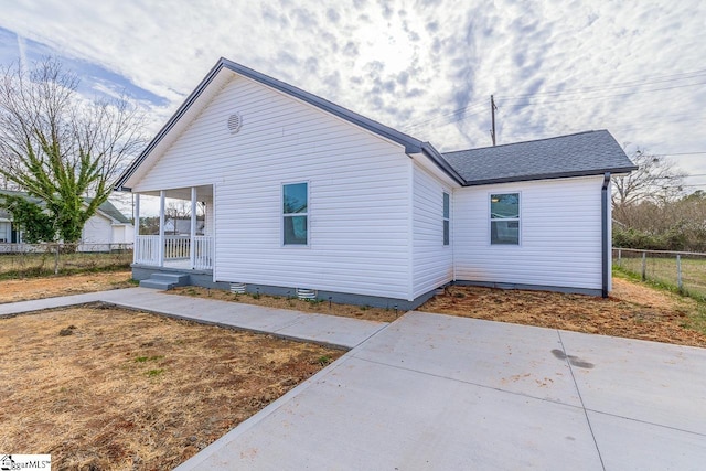 exterior space with roof with shingles, a porch, and fence