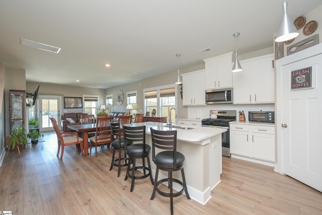 kitchen with visible vents, a kitchen island with sink, a sink, stainless steel appliances, and light wood-style floors