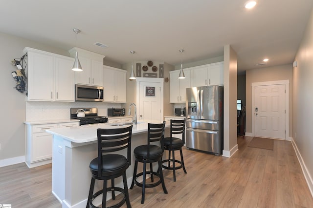 kitchen featuring visible vents, a kitchen island with sink, a sink, light countertops, and appliances with stainless steel finishes