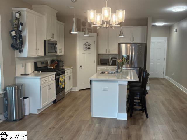 kitchen with a sink, stainless steel appliances, light countertops, white cabinets, and light wood-type flooring