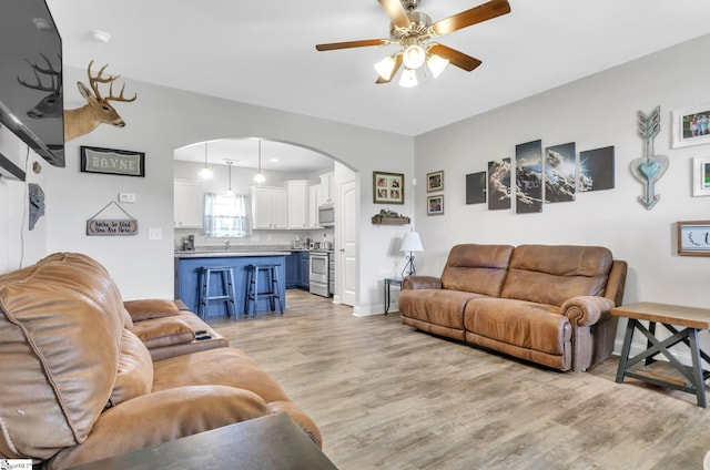 living room featuring baseboards, arched walkways, light wood finished floors, and ceiling fan