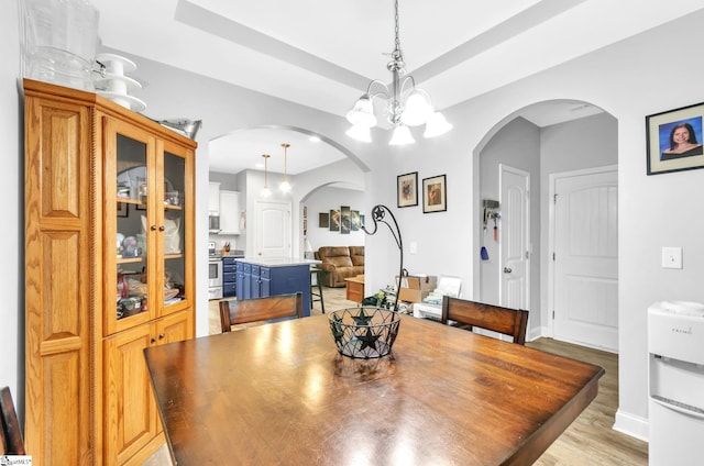 dining space featuring a raised ceiling, a notable chandelier, light wood-style floors, and arched walkways