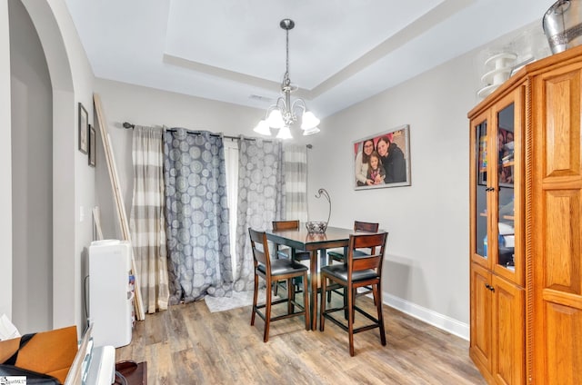 dining room with light wood-style flooring, a tray ceiling, arched walkways, baseboards, and a chandelier