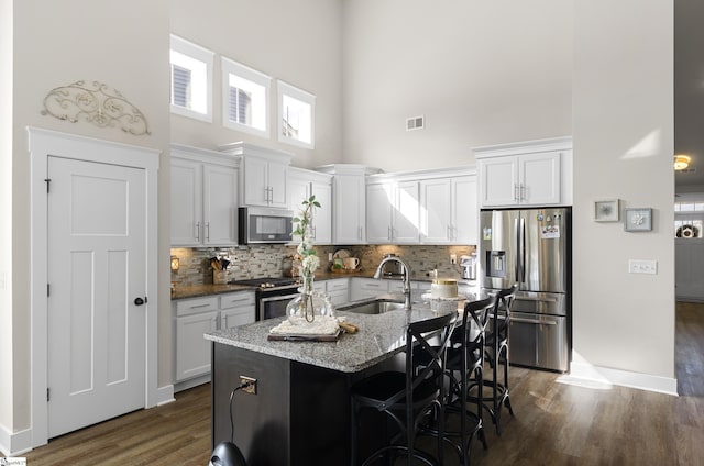 kitchen with light stone counters, a kitchen breakfast bar, a high ceiling, stainless steel appliances, and a sink