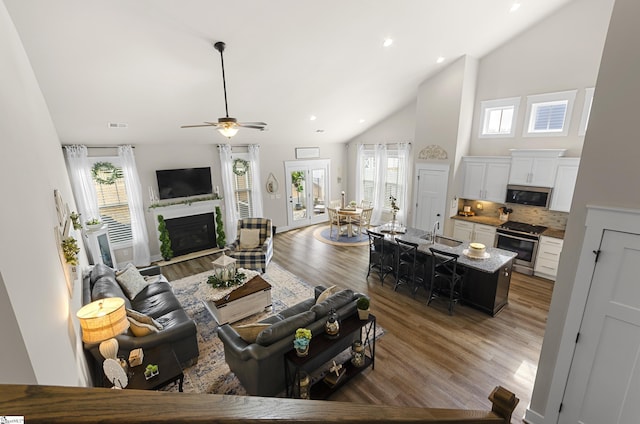 living room featuring high vaulted ceiling, light wood-style flooring, recessed lighting, ceiling fan, and a glass covered fireplace