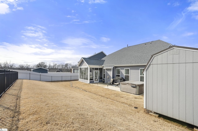 rear view of property featuring a patio, roof with shingles, a fenced backyard, a sunroom, and an outdoor structure