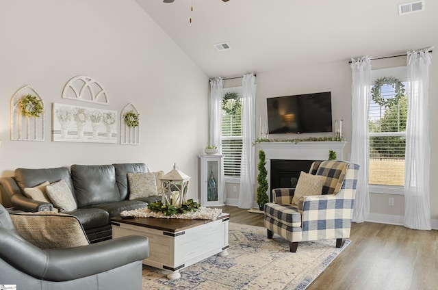 living area featuring visible vents, a ceiling fan, light wood-style floors, and a glass covered fireplace